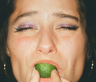 Close-up of a face with eyes squeezed shut, biting into a lime