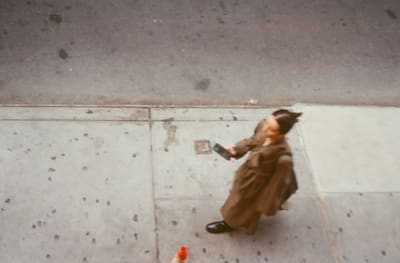Person in a long brown coat looking at a phone on the sidewalk below
