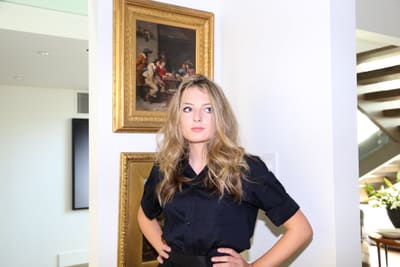 Model in a black shirt with hands on hips in front of gold-framed paintings