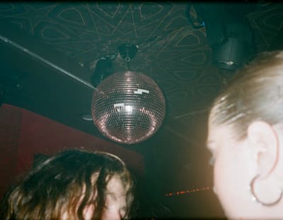 Disco ball hanging from a patterned club ceiling above two blurred heads in the foreground